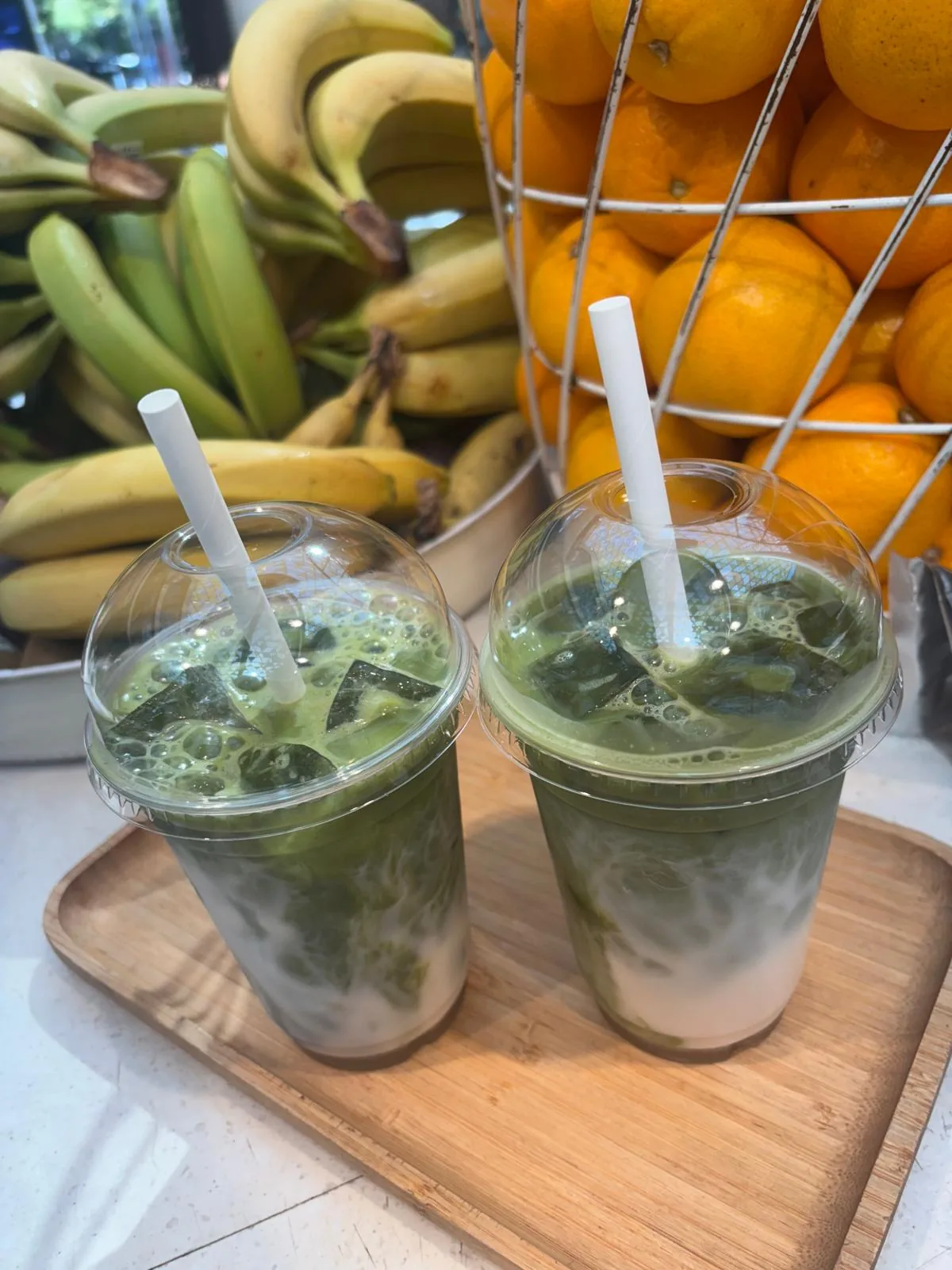 Deux matcha lattes glacés sur un plateau, devant les fruits frais du comptoir COFFEAT